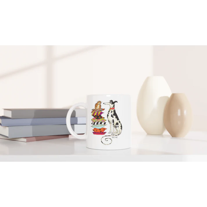 White mug with cat and spotted dog illustration on a shelf beside books and vases