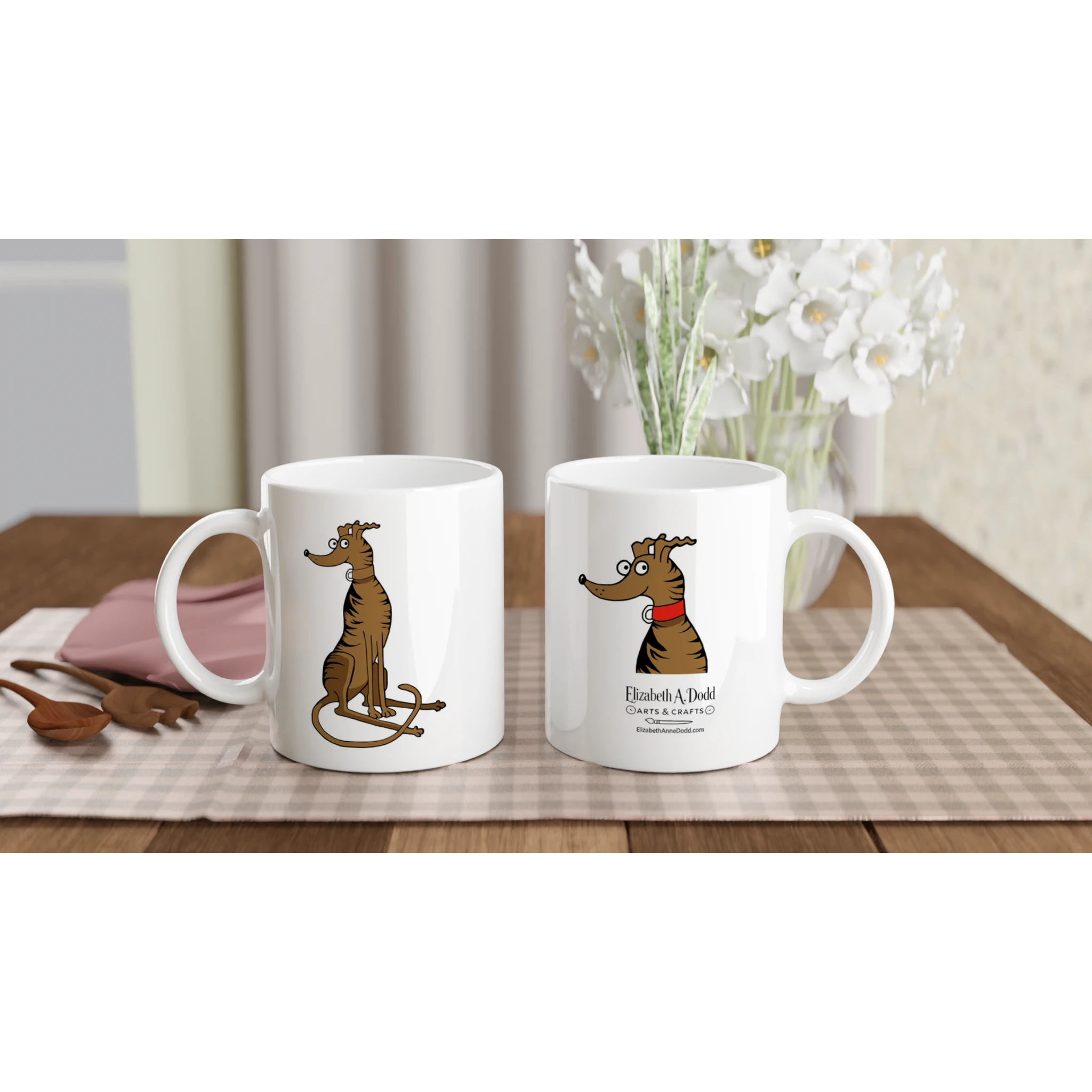 Two white mugs on a table, one with brindle greyhound illustration and one with logo