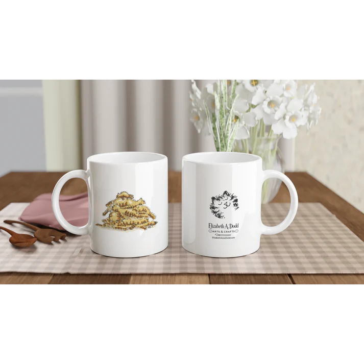 Two white mugs on a table, one showing a pile of cats illustration and one showing Elizabeth A. Dodd logo