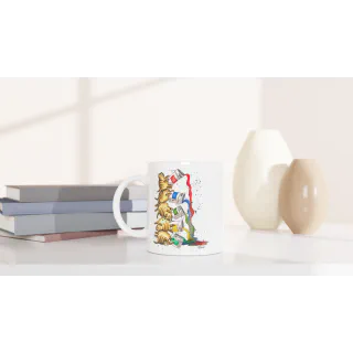 White mug with stacked tabby cats illustration on a tabletop beside books and vases