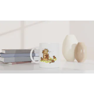 White ceramic mug with orange cat and kittens illustration on a tabletop beside books and vases