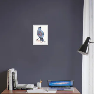 Small white framed kokako print above a desk with books and a laptop